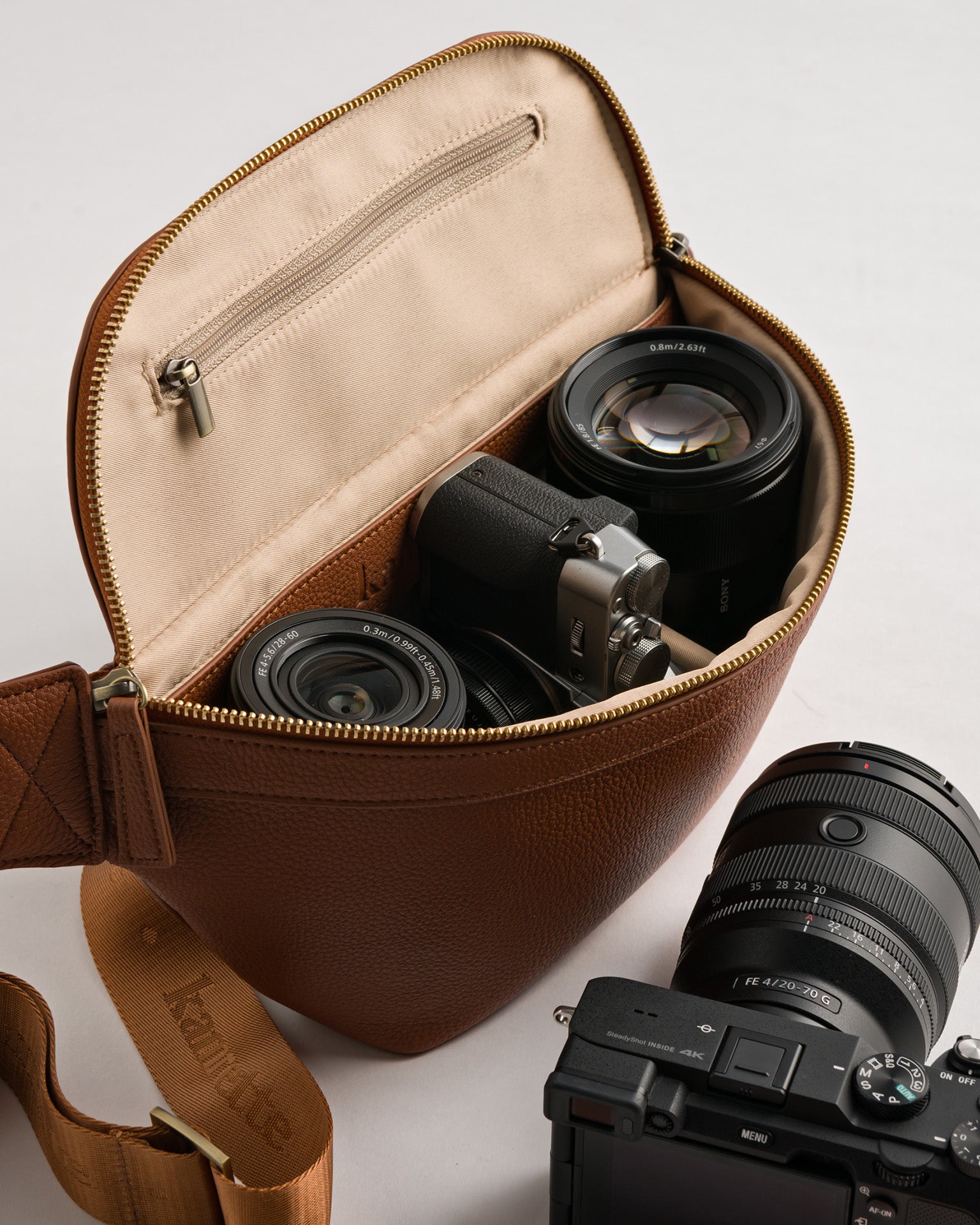 Fujifilm and Sony mirrorless camera and lenses inside padded Versa camera crossbody in Tan