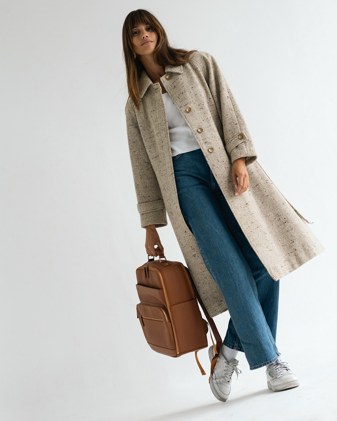Woman photographer holding handle of Lyra Camera Backpack in stylish outfit