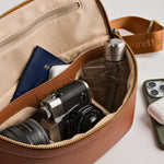 Padded interior of Versa crossbody with travel items including passport, mirrorless fujifilm camera and lens