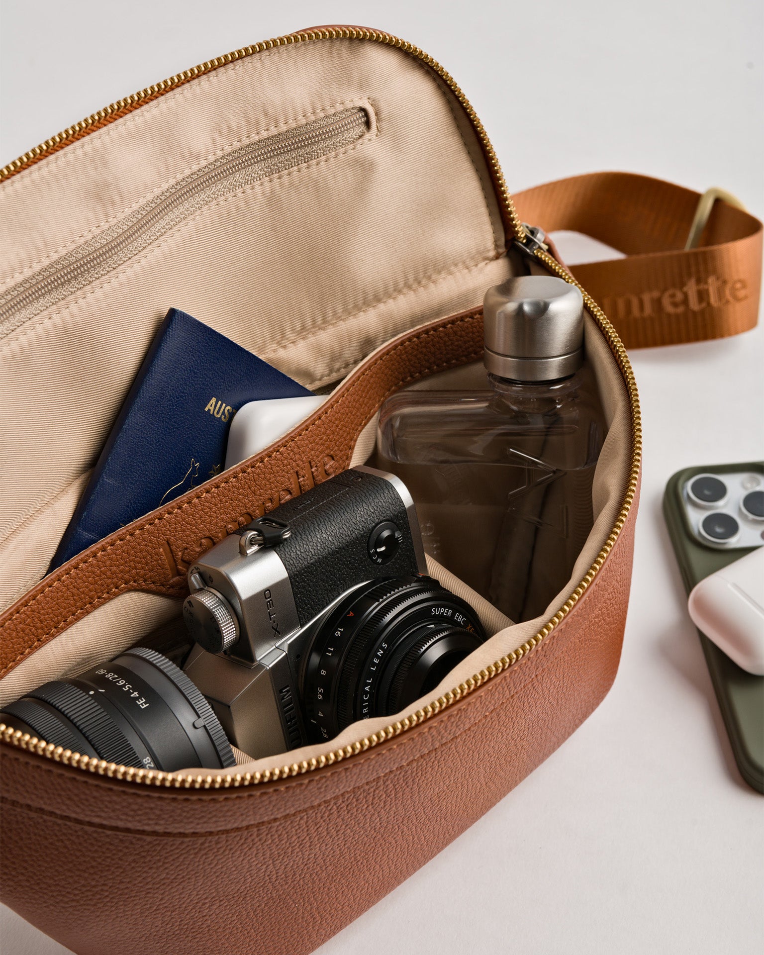 Padded interior of Versa crossbody with travel items including passport, mirrorless fujifilm camera and lens