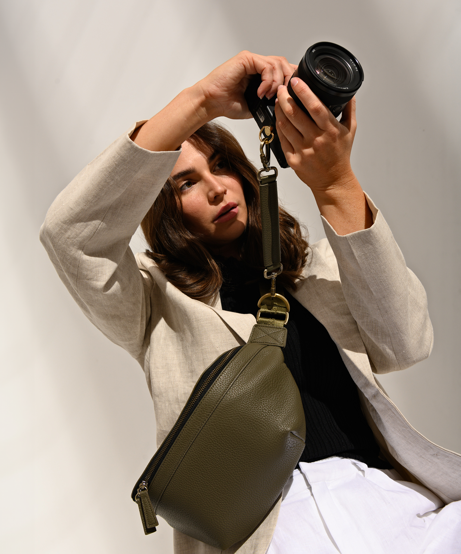 Woman photographer holding mirrorless camera attached to Versa Camera Bag using the camera strap