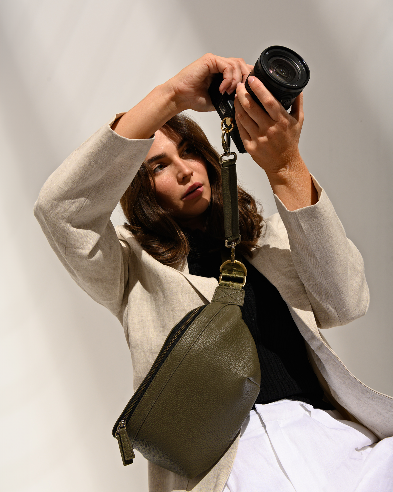 Woman photographer holding mirrorless camera attached to Versa Camera Bag using the camera strap