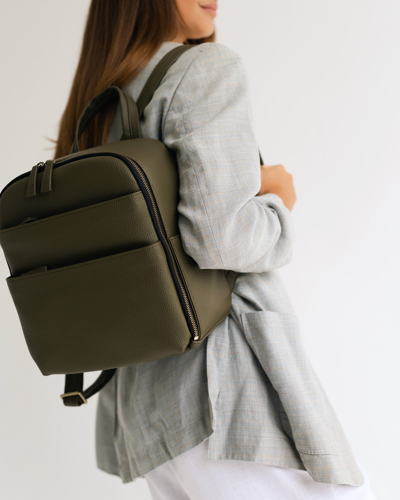 Woman photographer in stylish outfit wearing the Lyra camera backpack in Olive